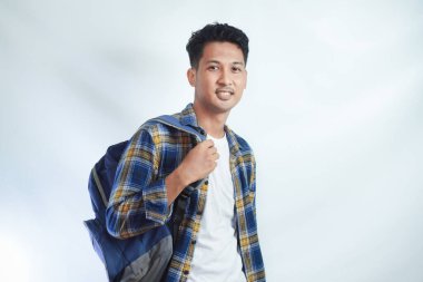 Sırt çantasıyla gülümseyen mutlu Asyalı genç erkek öğrenci beyaz arka planda yalnız başına okula hazır ve kendinden emin duruyor. Lise üniversite konsepti