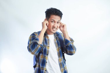 Sırt çantalı, kulakları kapalı, beyaz arka planda elleri izole genç Asyalı öğrenci. Lise üniversite konsepti