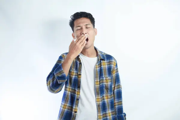 Portrait of exhausted and sleepy young student handsome man yawning standing on white isolated background in studio. Bored male feels sleepy, yawns as feels tired, opens mouth widely, closed eyes.