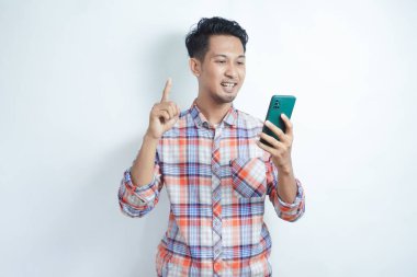 Yetişkin bir adam cep telefonunu tutarken parmağını kaldırarak mutlu bir ifade sergiliyor.