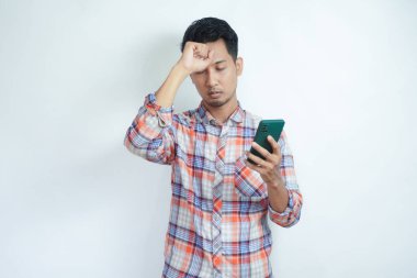 Asyalı adam cep telefonunu üzgün bir ifadeyle tutuyor.