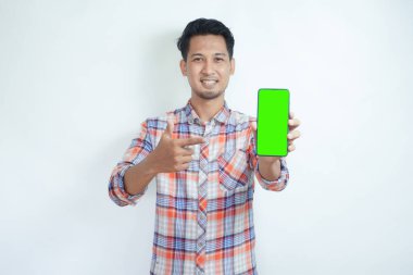 Adult Asian man smiling happy while showing green mobile phone screen and pointing on it clipart