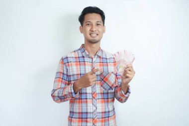Yetişkin Asyalı adam elinde kağıt para tutarken mutlu gülümsüyor ve onu işaret ediyor.