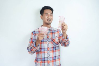 Yetişkin Asyalı adam elinde para tutarken mutlu bir şekilde gülüyor.