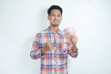 Yetişkin bir Asyalı, kağıt para tutarken ve mutlu bir ifade sergilerken yumruğunu sıktı.