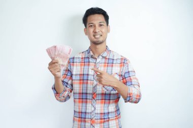 Yetişkin Asyalı adam elinde kağıt para tutarken mutlu gülümsüyor ve onu işaret ediyor.