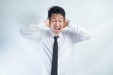 Yetişkin Asyalı bir adam elleriyle kulaklarını kapatır ve kızgın yüz ifadesi gösterir.