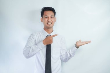 Yetişkin Asyalı adam sağ eli açık sol avucunu işaret ederek gülümsüyor.