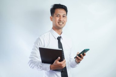 Yetişkin Asyalı bir adam elinde telefon ve kitap tutarken kameraya gülümsüyor.