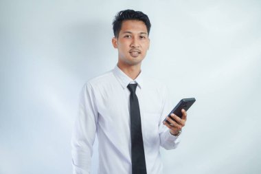 Adult Asian man smiling friendly when holding his mobile phone clipart