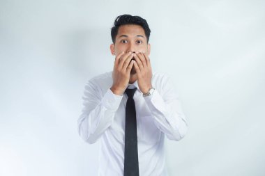 Dehşete düşmüş genç Asyalı iş adamının suratını örten ve yüzünde korkmuş bir ifadeyle kameraya bakan, işteki başarısızlıktan korkan fotoğrafı.