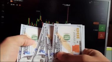 Adamın elleri bir dizüstü bilgisayarın arka planında üzerinde tırnak işareti olan dolar banknotlarını sayıyor.