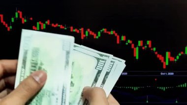 Adamın elleri bir dizüstü bilgisayarın arka planında üzerinde tırnak işareti olan dolar banknotlarını sayıyor.