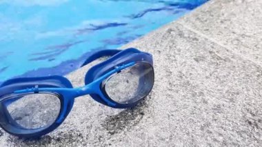 Mavi profesyonel yüzme gözlükleri ve gri havuz zeminindeki sarı lenslere su damlaları..