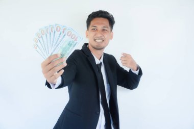 Takım elbiseli heyecanlı bir gencin portresi beyaz arka planda izole edilmiş bir sürü para banknotunu işaret ediyor.