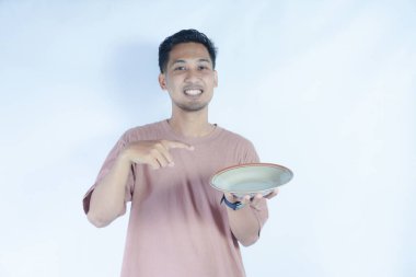 Pembe tişört giyen Endonezyalı bir adamın portresi. Beyaz bir arka planda, elinde tuttuğu boş bir plakayı mutlulukla gösteriyor..