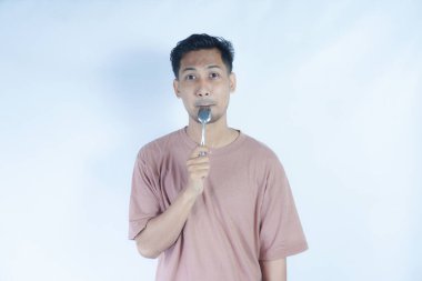 Tutkulu genç Asyalı adam beyaz arka planda izole edilmiş yemekleri tatmak için elinde pembe bir kaşık tutuyor. Halk Yaşam Tarzı Konsepti