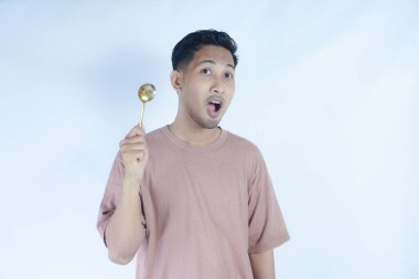 Tutkulu genç Asyalı adam beyaz arka planda izole edilmiş yemekleri tatmak için elinde pembe bir kaşık tutuyor. Halk Yaşam Tarzı Konsepti