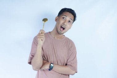 Tutkulu genç Asyalı adam beyaz arka planda izole edilmiş yemekleri tatmak için elinde pembe bir kaşık tutuyor. Halk Yaşam Tarzı Konsepti