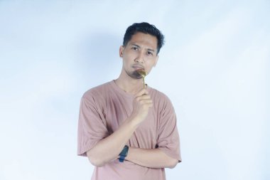 Tutkulu genç Asyalı adam beyaz arka planda izole edilmiş yemekleri tatmak için elinde pembe bir kaşık tutuyor. Halk Yaşam Tarzı Konsepti