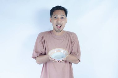Pembe t-shirt giyen Endonezyalı bir adamın portresi. Beyaz bir arka planda, elinde tuttuğu boş bir kâseyi mutlulukla gösteriyor..