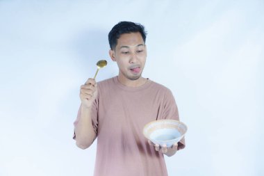 Pembe tişört giyen Endonezyalı bir adamın portresi, yeşil bir arka planda izole edilmiş bir kaşık ve kâseyle mutlu poz verirken ve yemeğin tadını çıkarırken görülüyor..