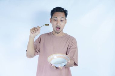 Pembe tişört giyen Endonezyalı bir adamın portresi, yeşil bir arka planda izole edilmiş bir kaşık ve kâseyle mutlu poz verirken ve yemeğin tadını çıkarırken görülüyor..