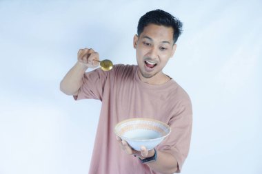 Pembe tişört giyen Endonezyalı bir adamın portresi, yeşil bir arka planda izole edilmiş bir kaşık ve kâseyle mutlu poz verirken ve yemeğin tadını çıkarırken görülüyor..