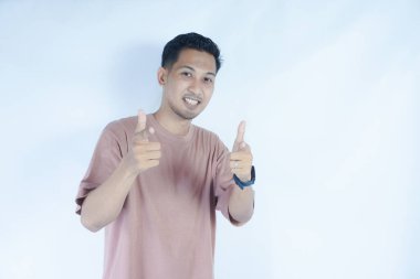 Pembe tişörtlü bir adam heyecanlı bir şekilde iki eliyle, ağzı açık bir şekilde şaşkınlıkla ve şaşkınlıkla onu işaret eder. Açık mavi arka plan, onun hareketli ve coşkulu ifadesini vurguluyor..