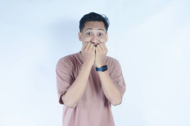 Pembe tişörtlü Asyalı adam gergin ve endişeli bir ifade sergiliyor. Elleri ağzının yanında, duruşu ve yüz ifadesi...