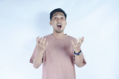 Pembe tişörtlü Asyalı bir adam, düz bir arkaplan karşısında duruyor, şaşırmış bir ifade ve yüzüne yakın duran eller. Görüntü bir şok ya da şaşkınlık anını yakalar. Yukarı bakıyorum.