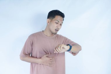 Pembe tişörtlü Asyalı bir adam saatini hafif bir gülümsemeyle kontrol ediyor, biraz eğlenmiş ya da saati merak ediyor gibi görünüyor. Açık mavi arka plan onun rahat ve ilgili tavrını vurguluyor..
