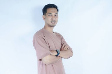 Pembe gömlekli Asyalı bir adam kollarını kavuşturup kameraya samimi bir şekilde gülümsüyor. Açık mavi arka plan onun rahat ve cana yakın tavrını vurguluyor..