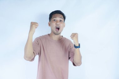 Pembe gömlekli bir adam kutlama jesti için iki elini de kaldırır, yüzü heyecan ve neşe içinde ışıldar. Açık mavi arka plan onun zafer ve coşkulu ifadesini vurguluyor..