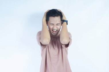 Pembe gömlekli bir adam başını acı dolu bir ifadeyle tutar. Baş ağrısı ya da rahatsızlık gösterir. Açık mavi arka plan sıkıntısını vurguluyor ve duruşunu ve ifadesini vurguluyor.