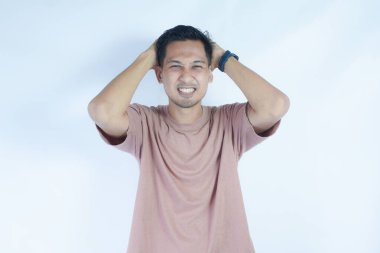 Pembe gömlekli bir adam başını acı dolu bir ifadeyle tutar. Baş ağrısı ya da rahatsızlık gösterir. Açık mavi arka plan sıkıntısını vurguluyor ve duruşunu ve ifadesini vurguluyor.