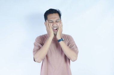 Pembe gömlekli bir adam çenesini acı dolu bir ifadeyle tutar. Bu da diş ağrısı ya da rahatsızlık gösterir. Açık mavi arka plan sıkıntısını vurguluyor ve duruşunu ve ifadesini vurguluyor.