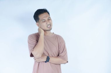 Pembe tişörtlü bir adam omzunu kederli bir ifadeyle tutarak omuz ağrısı ya da rahatsızlığı gösterir. Açık mavi arka plan sıkıntısını vurguluyor.