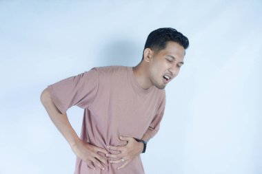 Pembe gömlekli bir adam, midesi ağrıyan bir yüz ifadesiyle karnını tutar. Bu da mide ağrısı ya da rahatsızlık gösterir. Açık mavi arka plan sıkıntısını vurguluyor.