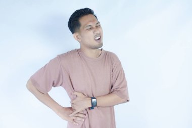 Pembe gömlekli bir adam hafifçe eğilir ve belini ağrılı bir ifadeyle tutar, sırt ağrısı ya da rahatsızlığı gösterir. Açık mavi arka plan sıkıntısını vurguluyor.