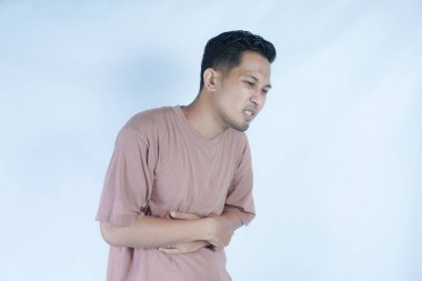 Pembe tişörtlü bir adam omzunu kederli bir ifadeyle tutarak omuz ağrısı ya da rahatsızlığı gösterir. Açık mavi arka plan sıkıntısını vurguluyor.