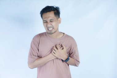 Pembe gömlekli bir adam göğsünü iki eliyle kavrıyor. Acı dolu bir yüz ifadesi sergiliyor. Muhtemelen göğüs ağrısı ya da rahatsızlığı gösteriyor. Açık mavi arka plan sıkıntısını vurguluyor.