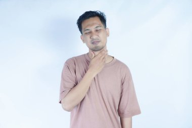 Pembe tişörtlü bir adam boğazı ağrıyan bir boğaz ya da rahatsızlığı gösteren acı dolu bir ifadeyle boğazını tutar. Açık mavi arka plan sıkıntısını ve önemli noktaları vurguluyor.