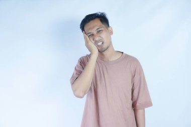 Pembe gömlekli bir adam çenesini acı dolu bir ifadeyle tutar. Bu da diş ağrısı ya da rahatsızlık gösterir. Açık mavi arka plan sıkıntısını vurguluyor ve duruşunu ve ifadesini vurguluyor.