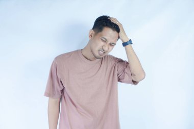 Pembe gömlekli bir adam başını acı dolu bir ifadeyle tutar. Baş ağrısı ya da rahatsızlık gösterir. Açık mavi arka plan sıkıntısını vurguluyor ve duruşunu ve ifadesini vurguluyor.