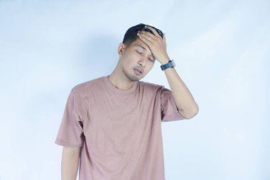 Pembe gömlekli bir adam başını acı dolu bir ifadeyle tutar. Baş ağrısı ya da rahatsızlık gösterir. Açık mavi arka plan sıkıntısını vurguluyor ve duruşunu ve ifadesini vurguluyor.