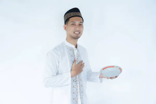 stock image Moslem man touching his stomach with happy relieved expression while holding empty dinning plate