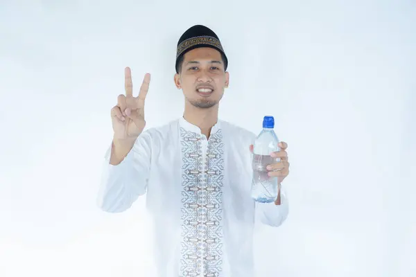 stock image Moslem Asian man smiling and showing two fingers while holding a drinking water bottle