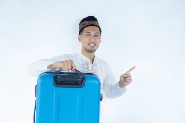 Müslüman Asyalı adam kameraya gülümsüyor ve bavul taşırken sağ tarafı gösteriyor.