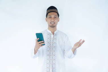 Moslem man smiling to camera while holding mobile phone clipart